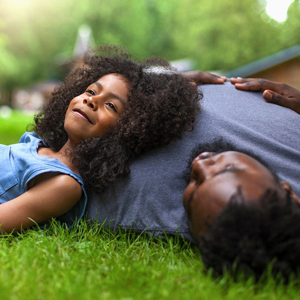 African-American son and father rests on grass at backyard holiday villa
